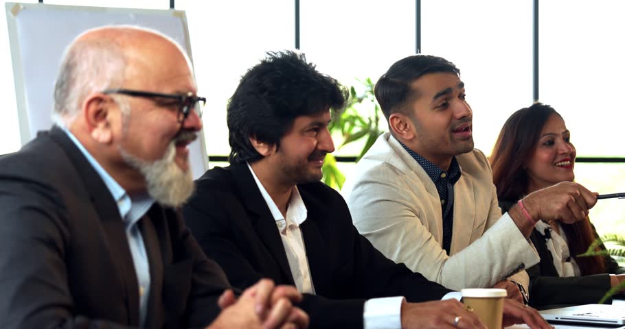 Indian Asian group of four successful business professionals in executive attire, sitting at one side of the conference table, discussing or interviewing someone