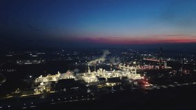 oil refinery is visible against the background of blue sky with pink tint, illuminated by flickering lights.Plumes of smoke rise from the chimneys, emphasizing the activity of the enterprise at night  - Powered by Shutterstock - Get 15% off with code: PIKWIZARD15