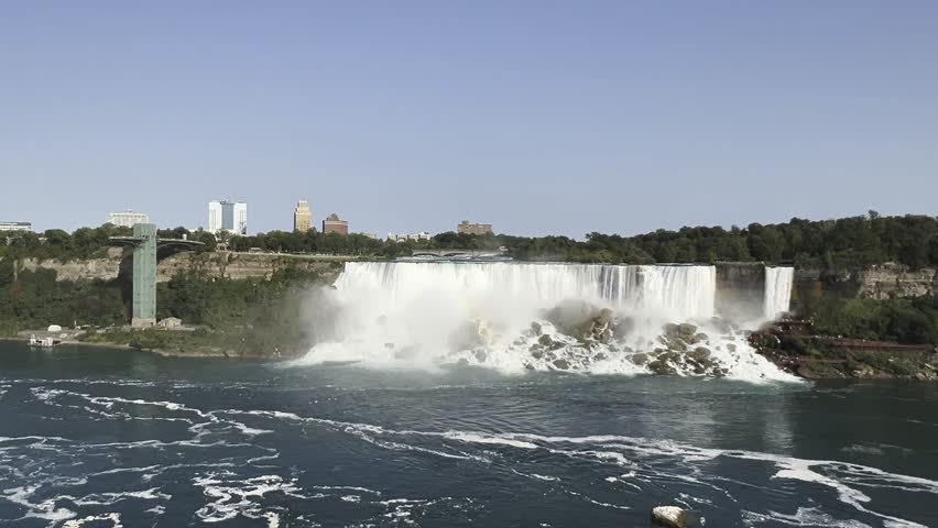 Establishing Shot of Niagara Falls Plunging into the Niagara River from the American Side, Featuring the Niagara Falls Observation Tower and the City Skyline on a Clear Sunny Day, Canada