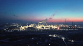 oil refinery is visible against the background of blue sky with pink tint, illuminated by flickering lights.Plumes of smoke rise from the chimneys, emphasizing the activity of the enterprise at night  - Powered by Shutterstock - Get 15% off with code: PIKWIZARD15