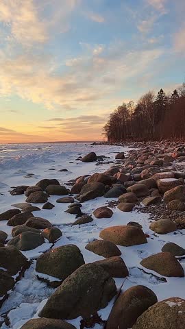 Winter landscape. Panoramic view of beautiful sunset on bay. List clouds over water in bright light. Ice, snow and rocks on coastline. Setting sun is reflected in sea. High quality footage