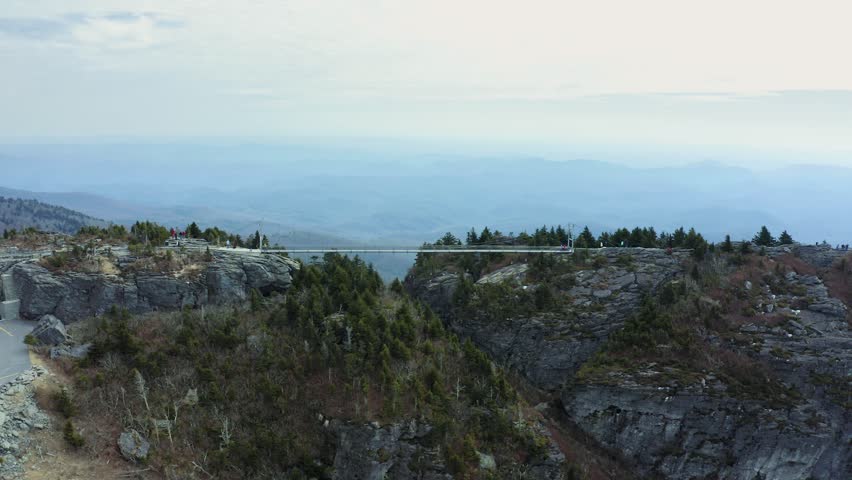 Aerial dolly to bridge connecting ridge peaks in Grandfather Mountain Nature Park, North Carolina, showcasing scenic mountain landscapes