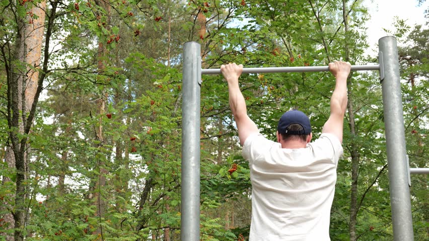 Man in white t-shirt doing chin up excercise at outdoors. Active lifestyle concept.