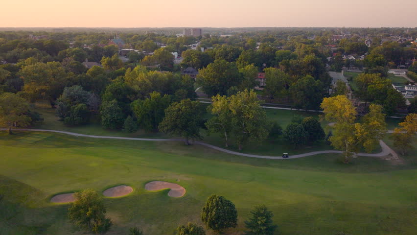 Beautiful aerial over Forest Park Golf Course toward houses on Lindell Blvd in St. Louis at sunset. Captures golden hour light, lush fairways, and city charm. Perfect for real estate and travel.