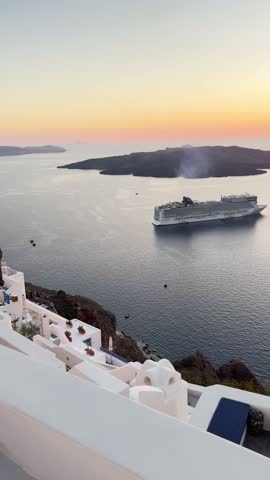 Beautiful sunset in Santorini island, Greece. White architecture with sea view. Cruise ship near the coast. Blue sea and the blue sky at sunset. Summer travel and vacation. Vertical video
