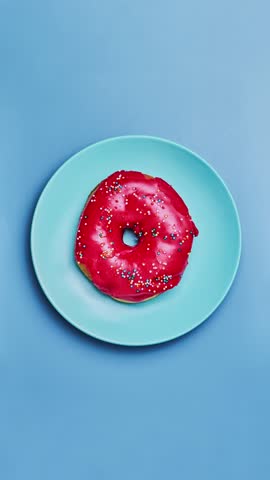 Pink donut on blue plate. Eating tasty donut. Top view. Stop motion of donut bite on blue background. Bakery and food concept in 4K, UHD
