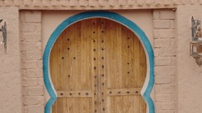 Traditional Moroccan wooden door with ornate metal studs in a peach-colored clay brick wall with a blue arch. A decorative metal lantern hangs beside the door. travel, culture, - Powered by Shutterstock - Get 15% off with code: PIKWIZARD15