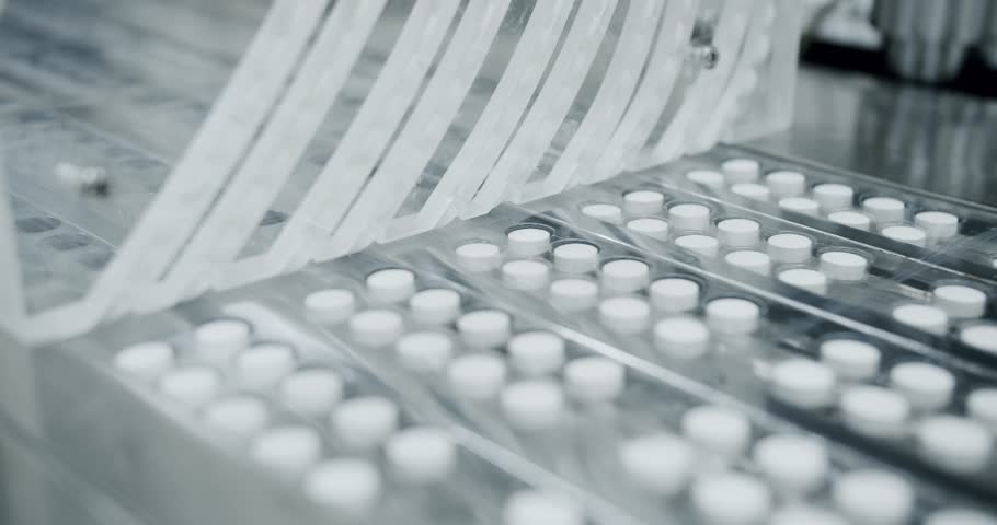 White pills moving on metal automatic line in workshop of pharmaceutical factory. Factory equipment and machine conveyor. Industrial pharmaceutical concept. view of drugs move along conveyor belt.