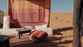Relaxing desert camp in Erg Chebbi, Sahara Desert, Merzouga, Morocco. A comfortable lounge area under a tent provides shade from the midday sun. Traditional Moroccan furniture and colorful textiles - Powered by Shutterstock - Get 15% off with code: PIKWIZARD15