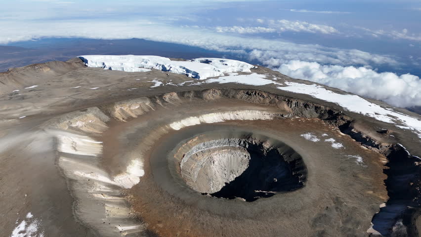 Drone shot of Uhuru Peak on Mount Kilimanjaro with the volcanic crater below. Revealing aerial shot