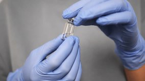 Medical professional wearing blue nitrile gloves handling small glass vial with clear liquid medication, highlighting sterile healthcare environment and precise medical preparation - Powered by Shutterstock - Get 15% off with code: PIKWIZARD15
