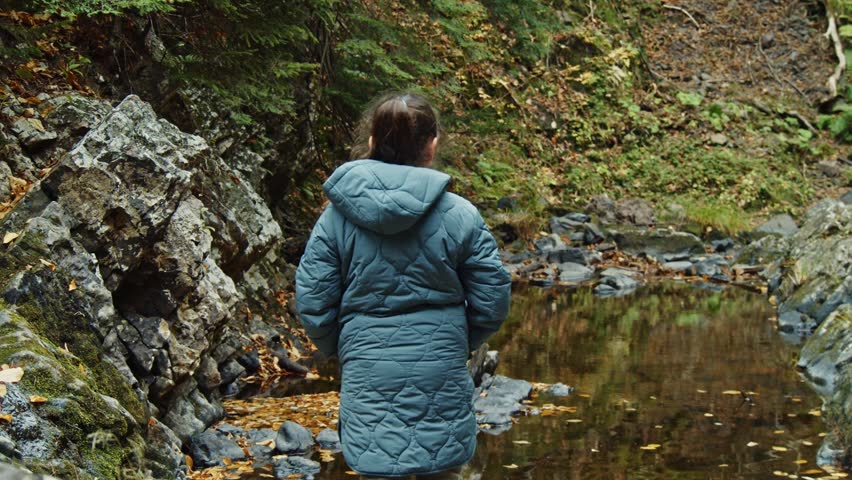 An Eight-Year-Old Girl Stands Still, Watching Waterfalls Cascade In A Mountain Forest. Her Warm Autumn Jacket Keeps Her Comfortable As She Takes In The Beautiful Surrounding Autumn Foliage.