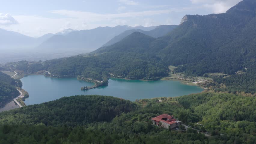 A drone shot of a lake, with a monastery on the foreground on a cloudy day