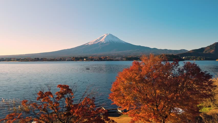 This stunning drone footage captures the serene beauty of Lake Kawaguchi at sunrise, surrounded by vibrant red autumn foliage and the majestic Mount Fuji in the background.