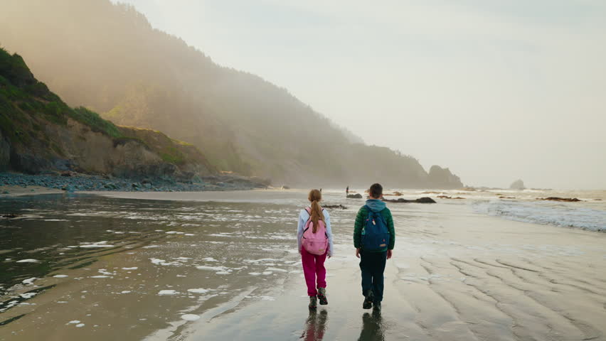 Siblings walking together along a quiet West Coast beach, enjoying the peaceful summer atmosphere and coastal scenery.