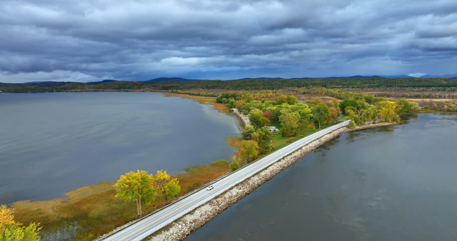 A highway crosses the river in Vermont, New England, USA. Nature change colors in autumn. Grey dramatic cloudscape in the sky. Aerial view.