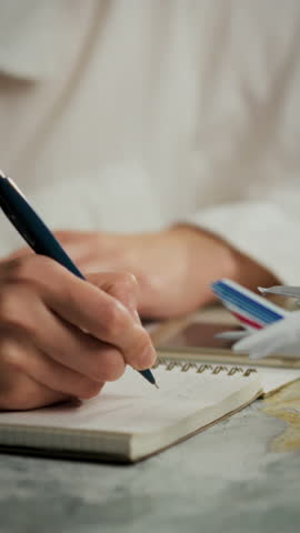 A person is focused on writing travel plans in a small notebook. Nearby, a model airplane adds a thematic touch to the planning process, highlighting aspirations for future journeys