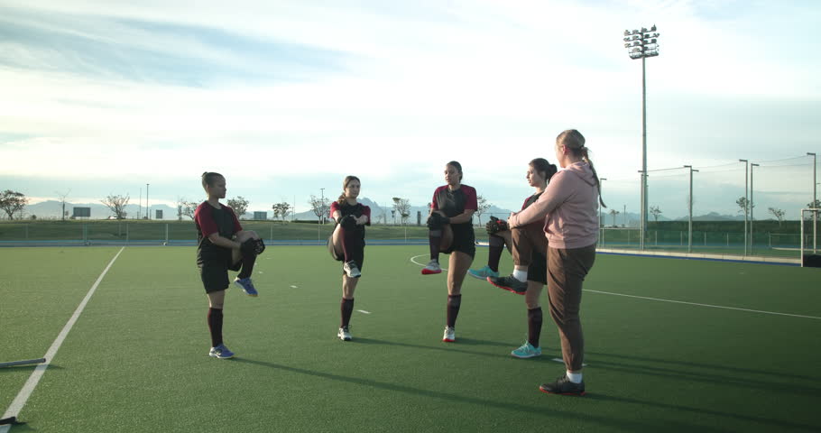 Female hockey team warming up with coach on outdoor field, preparing for practice. Teamwork, coaching, sports, exercise, training, field hockey