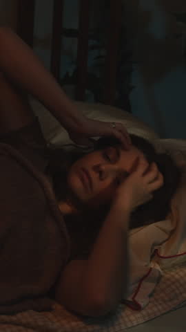 Vertical video. Young woman suffering from insomnia and headache lying in bed at night.