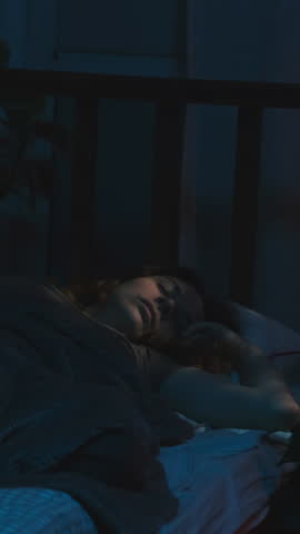 Vertical video. Sleepy woman wakes up early on weekday morning before dawn on an alarm clock.