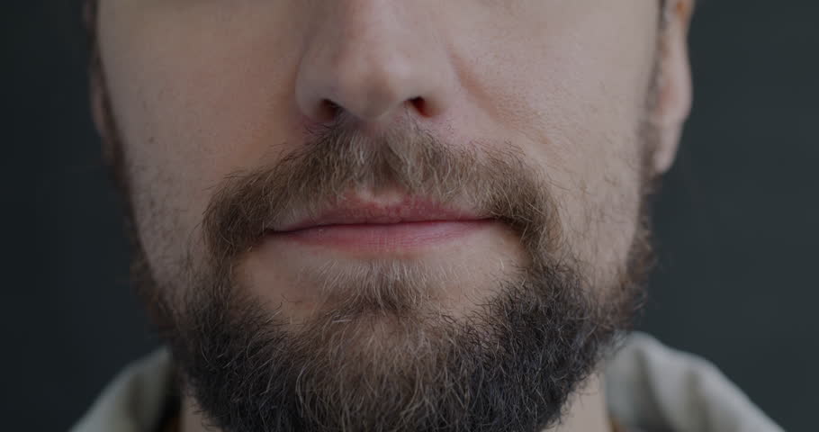 Close-up portrait of male mouth smiling while bearded man feeling happy on black color background. People and positive emotion concept.