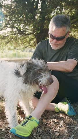 A man sits on the ground, interacting closely with his furry companion. They are surrounded by lush greenery in a bright and inviting park.