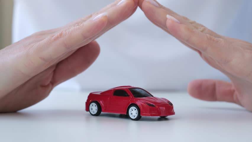 Concept of car protection and insurance. Female hands protecting red toy auto on white table