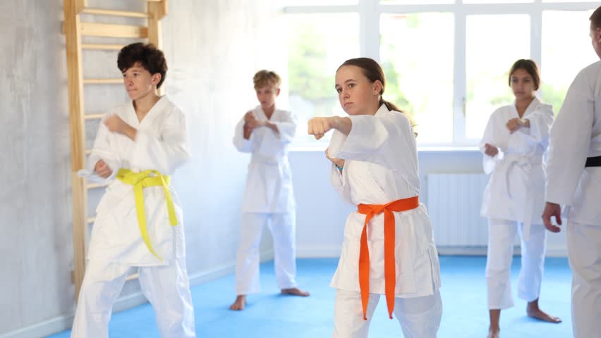 Group of boys and girls in kimonos train karate techniques in studio