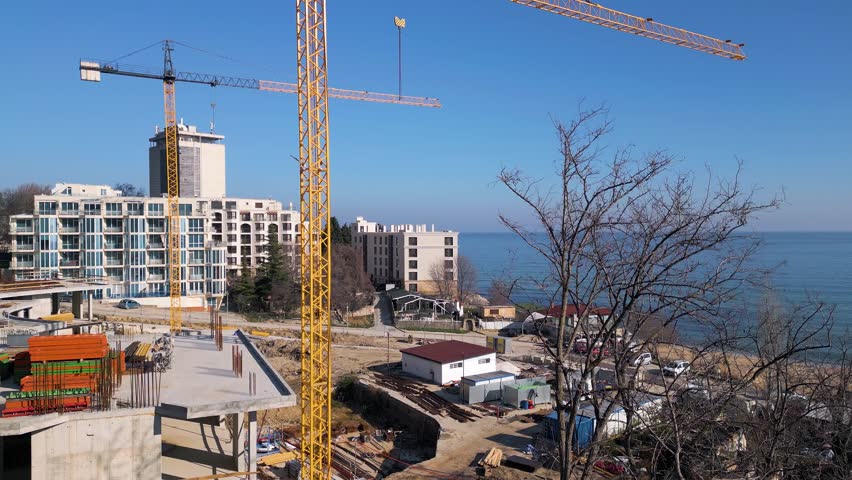 New hotel or residential complex under construction on the picturesque Kabakum Beach near Varna, Bulgaria. Tower cranes, metal structures, and the seaside view define this vibrant sunny worksite