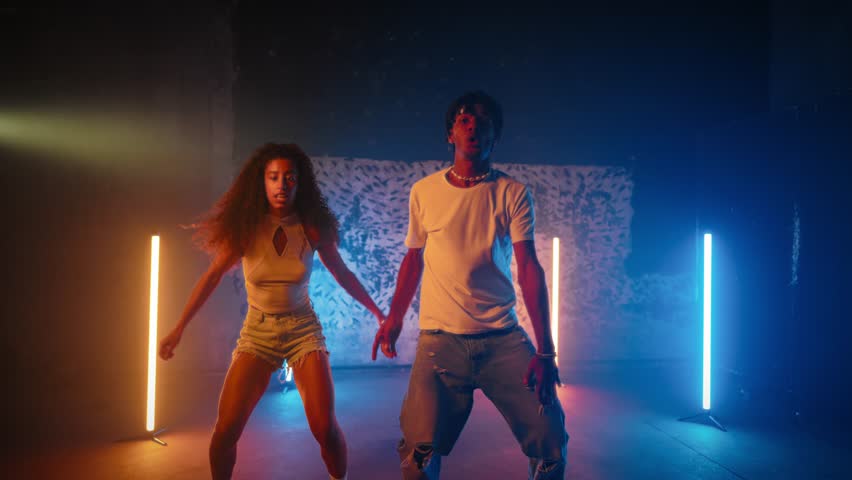 Dancehall performers moving synchronously in dance studio, black man and woman. Joyful young people enjoying music and rhythm, moving body and looking at camera, energy of motions, modern dance style