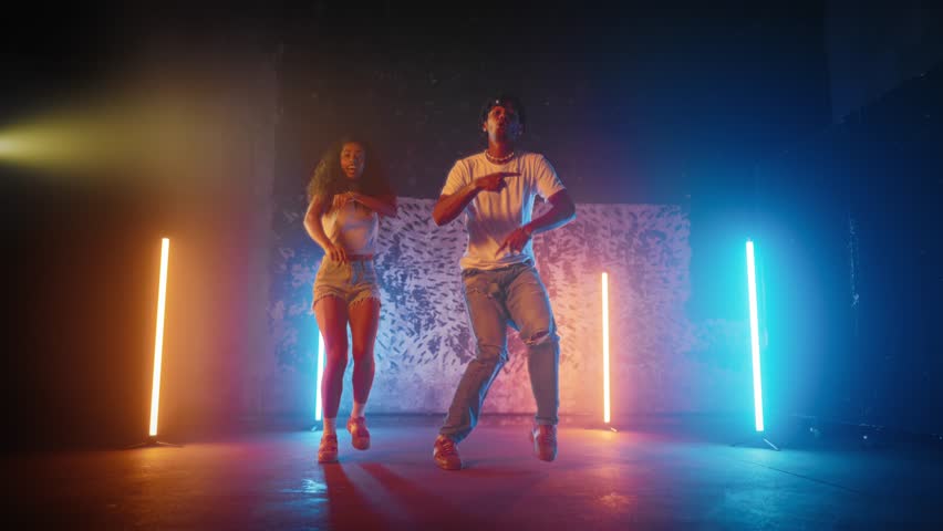 Positive male and female dancers moving actively on dance floor in studio. Full-length portrait of African American people jumping and dancing, good mood and emotions, creative hobby and leisure
