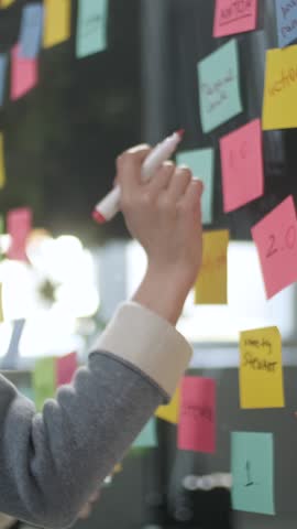 Asian Business Woman Write Tasks Creative Ideas On Sticky Notes On Glass Board, Female Corporate Leader Planning Project On Post It Sticky Notes Organize Work On Stickers