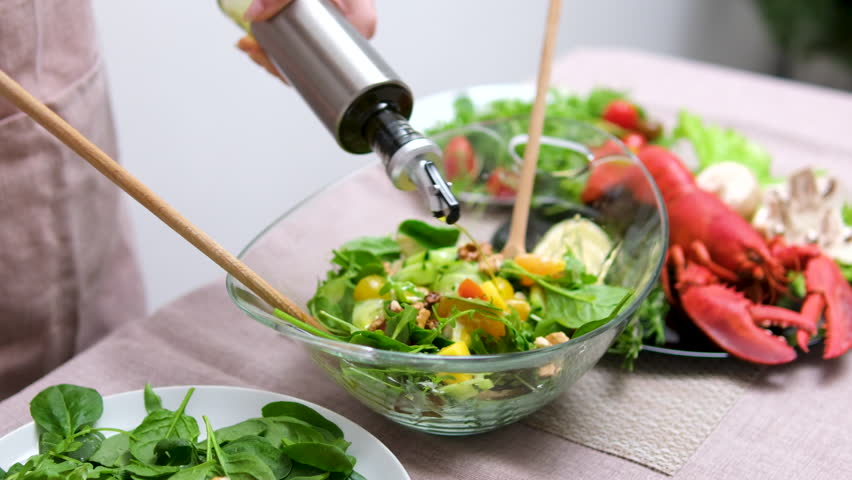 Couple cooking in the kitchen. womans hand preparing salad for dinner. Close up of a female preparing a vegetable salad. Olive oil for salad. Mix healthy vegetable salad. Healthy diet meal