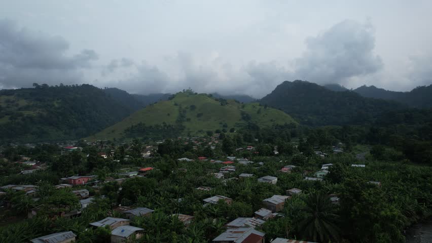 A drone shot of a quiet village in São Tomé, surrounded by trees and a mountain in the background.