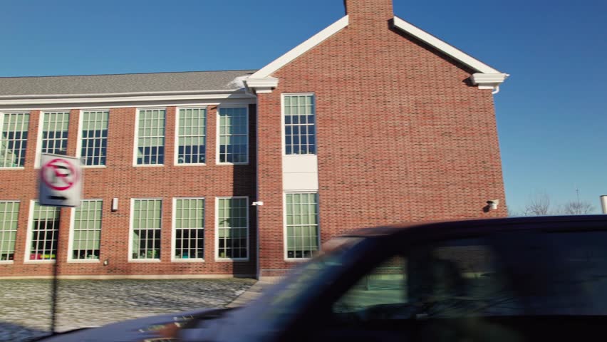 Driving past closed school and education brick building during a cold winter in Columbus Ohio as class is canceled and delayed by snow, ice, and low temperature weather from car pov point of view