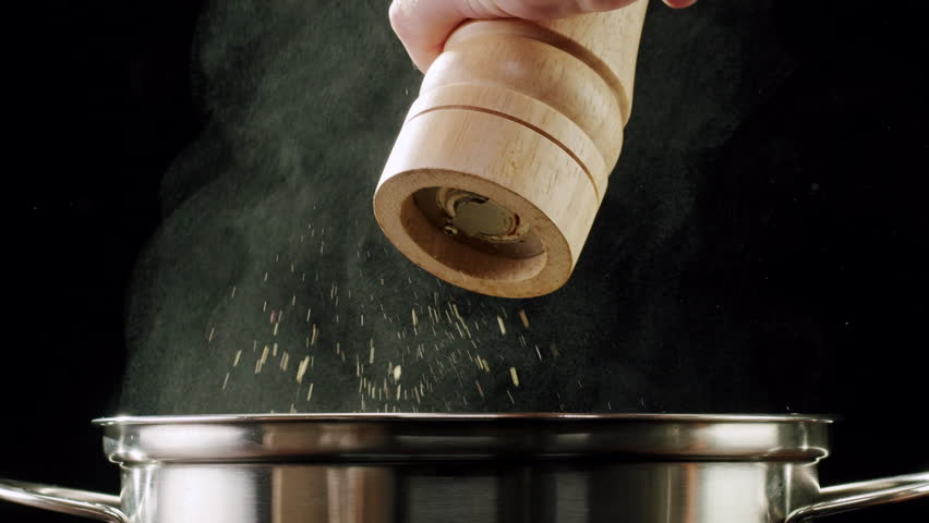 Professional chef adds pepper salt and curry curcuma indian peppers to a pot of boiling food. Restaurant kitchen cooking, colorful spices, dropping spices.