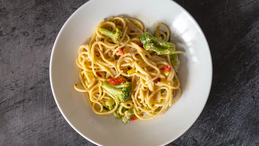 A Rotating Plate of Noodles with Vegetable and Cheese Sauce Shot from Above