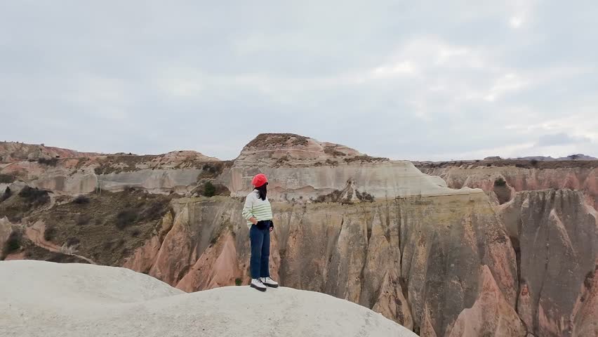 Inspirational aerial circular view Woman solo traveler on viewpoint in Cappadocia admire stunning rock formations. Colorful Rose and red valleys. Famous visit destination in Nevsehir. Anatolia