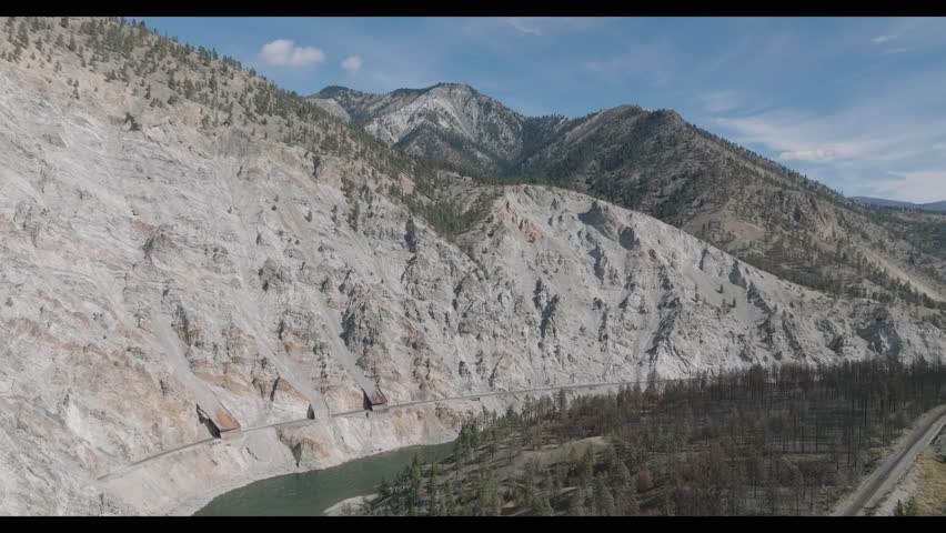 A landscape of dried rocky hills with white sand along Upper Fraser River under a blue sky