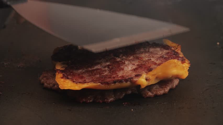 Cooking American fat smash burger with cheese slice on top on grill close-up. Beef or pork cutlet smashing by burger press. The chef in kitchen of the restaurant making cutlets for burgers - smash