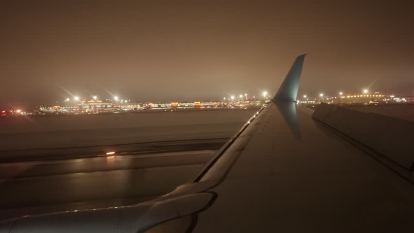 After landing plane moves along runway at night against background of bright airport lights. Plane with its flaps raised slows down on landing against background of another plane passing at high speed