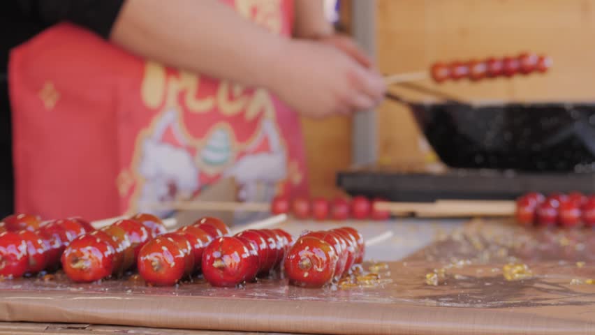 Making fruits in boiling caramel close-up. Chinese winter sweet dessert Tanghulu street food.Berries, grapes, tangerine and others fruit caramelized in sugar. Asian street market with traditional food
