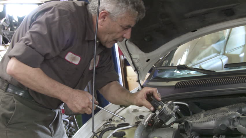 Auto mechanic working on the a car engine. Mid shot zooms into close up on