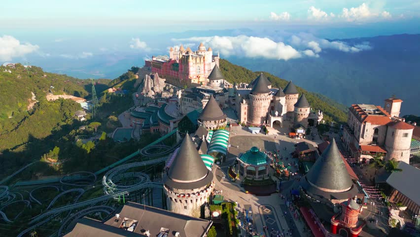 Aerial view of Ba Na Hills featuring a whimsical fairytale castles surrounded by lush greenery and mountains. Visitors can be seen enjoying the attractions.