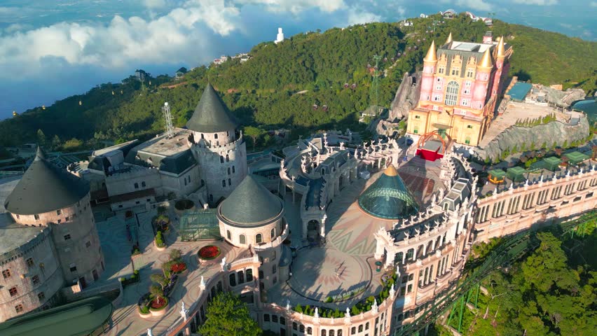Aerial view of the Ba Na Hills featuring a fairytale palace with castles surrounded by lush greenery and clouds.
