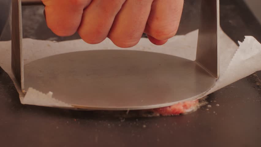 Cooking American fat smash burger on grill close-up. Beef or pork cutlet smashing by burger press. The chef in kitchen of the restaurant making cutlets for burgers - smash burger beefsteak. Fast and
