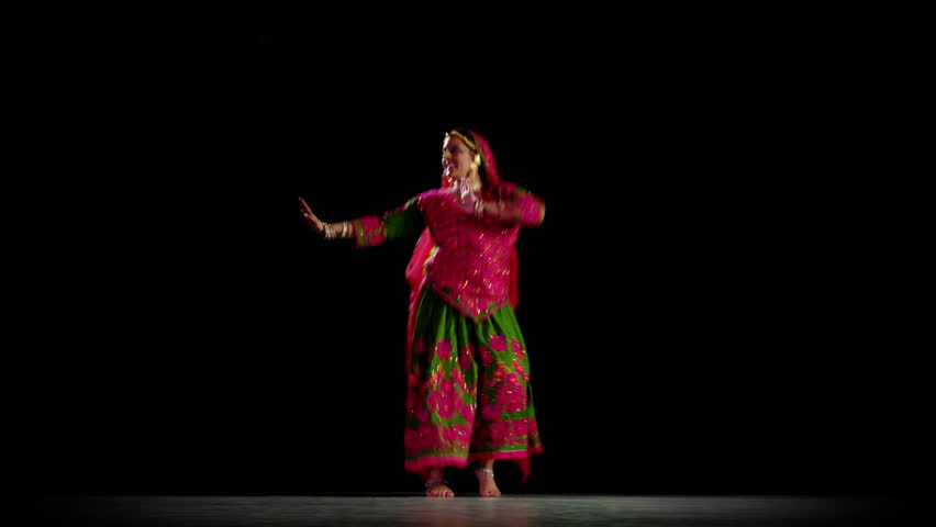 Indian girl in traditional dance costume dances against a black background. Full