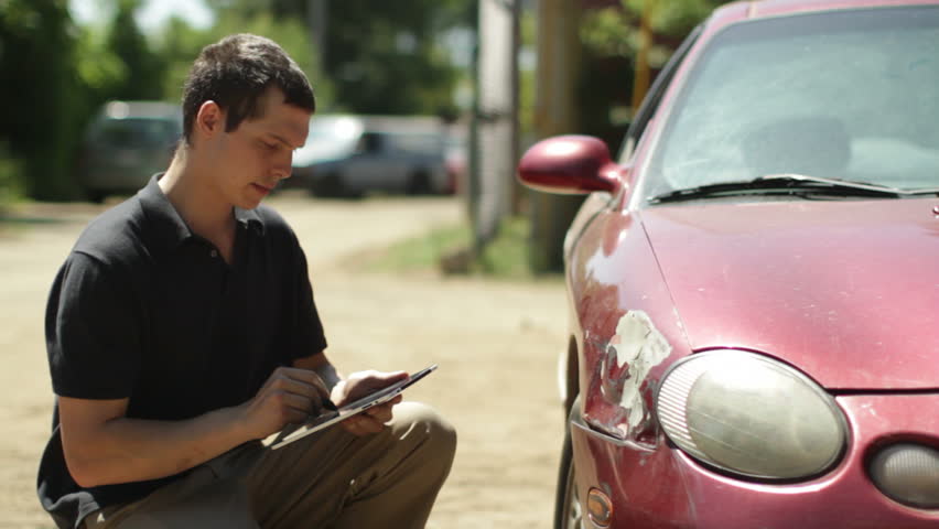 Insurance person inspects the damage on a car and makes notes on a digital