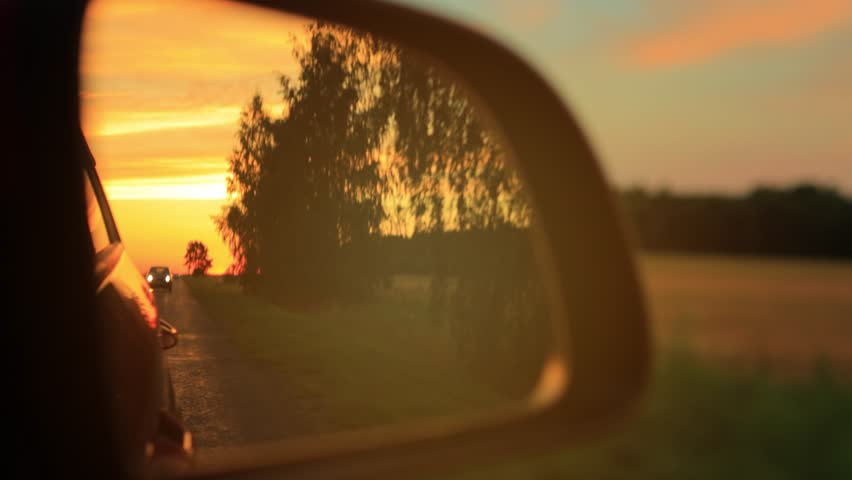 The sun is reflected in the mirror and window, evening road. View in the side rear view mirror of a car driving along the highway, in a red car	