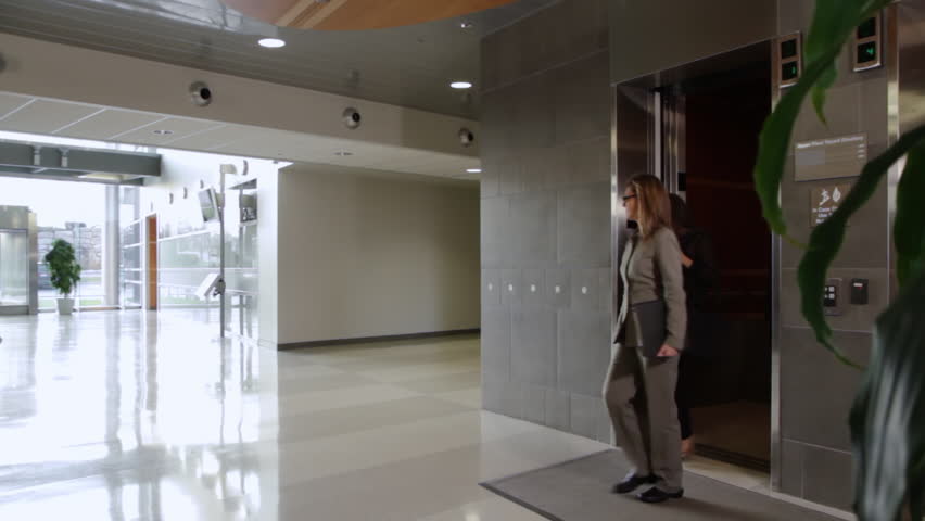 Business people get out of an elevator and walk through building atrium, towards